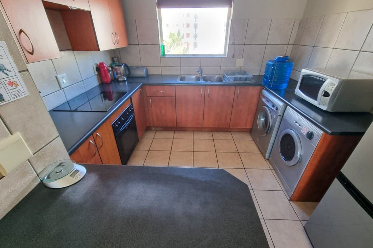 A functional kitchen featuring wood-finish cabinetry, dark laminate countertops, tiled backsplash, and integrated appliance spaces for a washing machine and tumble dryer.