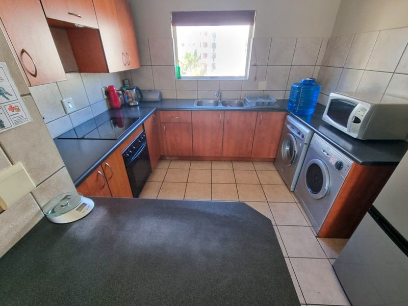 A functional kitchen featuring wood-finish cabinetry, dark laminate countertops, tiled backsplash, and integrated appliance spaces for a washing machine and tumble dryer.