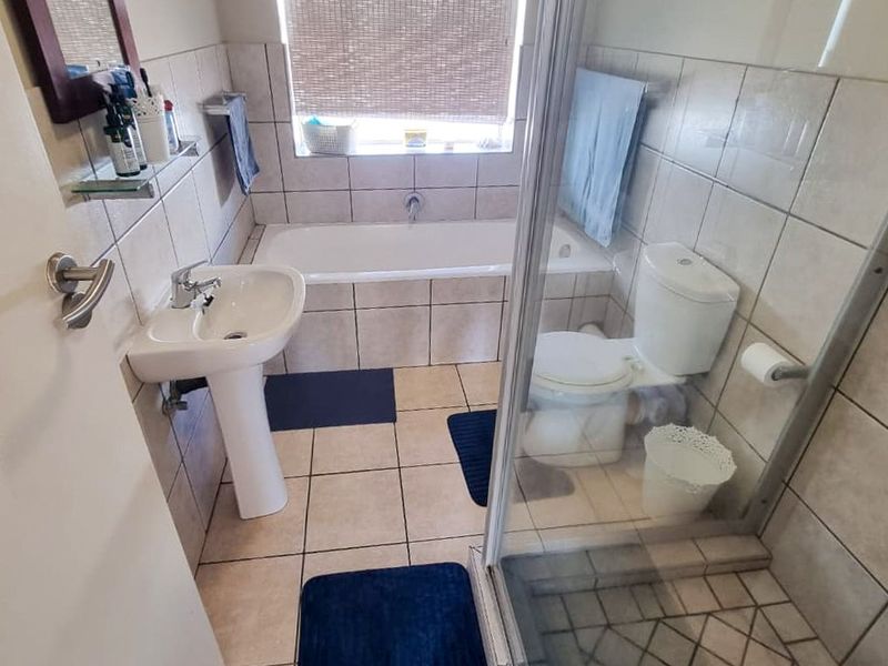 A functional bathroom featuring a pedestal basin, a built-in bathtub, and a separate glass-enclosed shower with neutral wall and floor tiling.