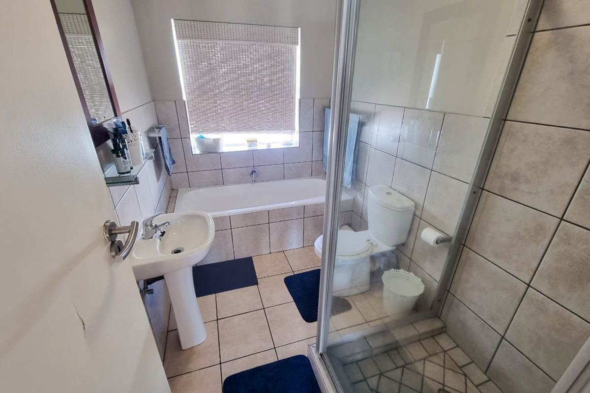 A functional bathroom featuring a pedestal basin, a built-in bathtub, and a separate shower enclosure with tiled finishes throughout.