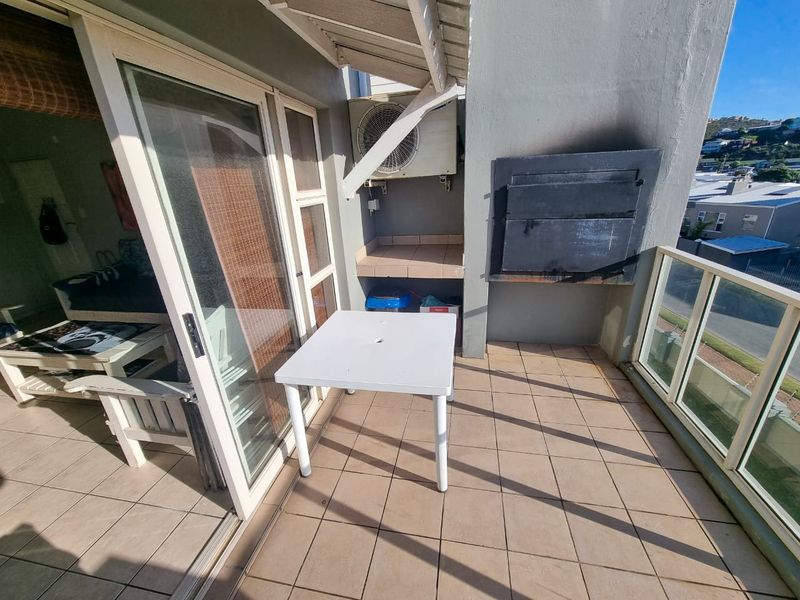 A balcony featuring tiled flooring, a built-in braai with visible soot staining, and a glass balustrade overlooking the surrounding area.