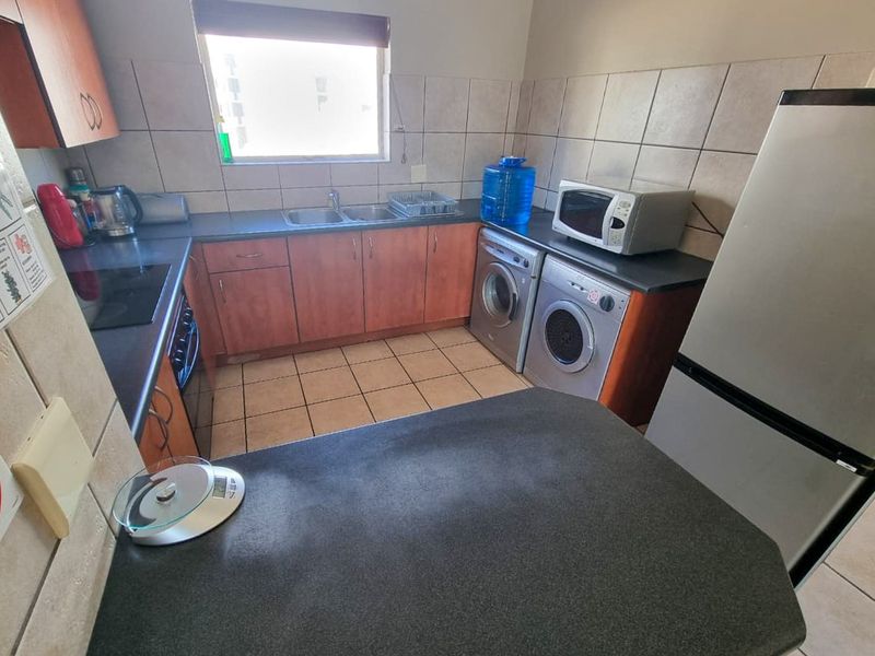 A functional kitchen featuring built-in wooden cabinetry, laminate countertops, a double basin sink, and tiled finishes, providing a practical workspace for daily needs.