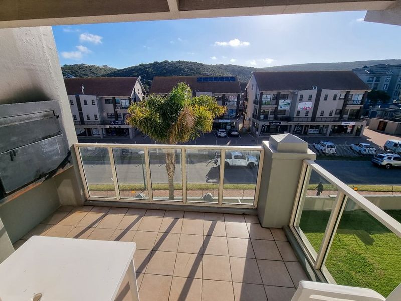 A covered balcony featuring tiled flooring, a built-in braai, and a glass balustrade overlooking the street and surrounding neighborhood.