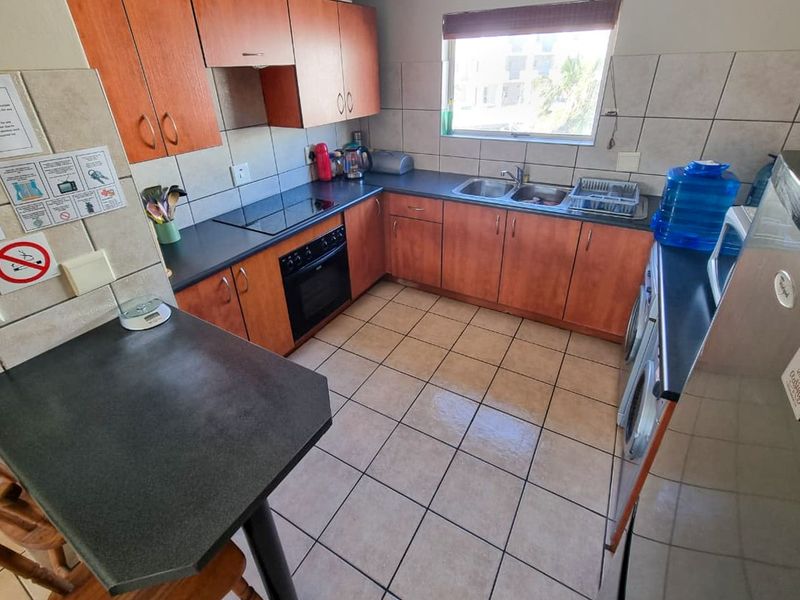 Functional kitchen featuring wood-look cabinetry, dark laminate countertops, tiled backsplash, and integrated appliances including an oven and hob.