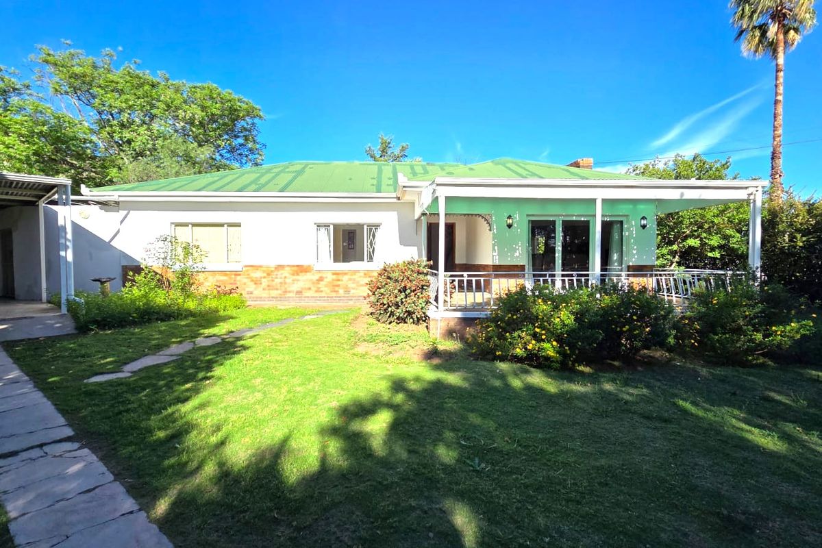 Rear view of the house featuring a covered patio, brick and plaster facade, metal roof, and an attached carport set within a garden.