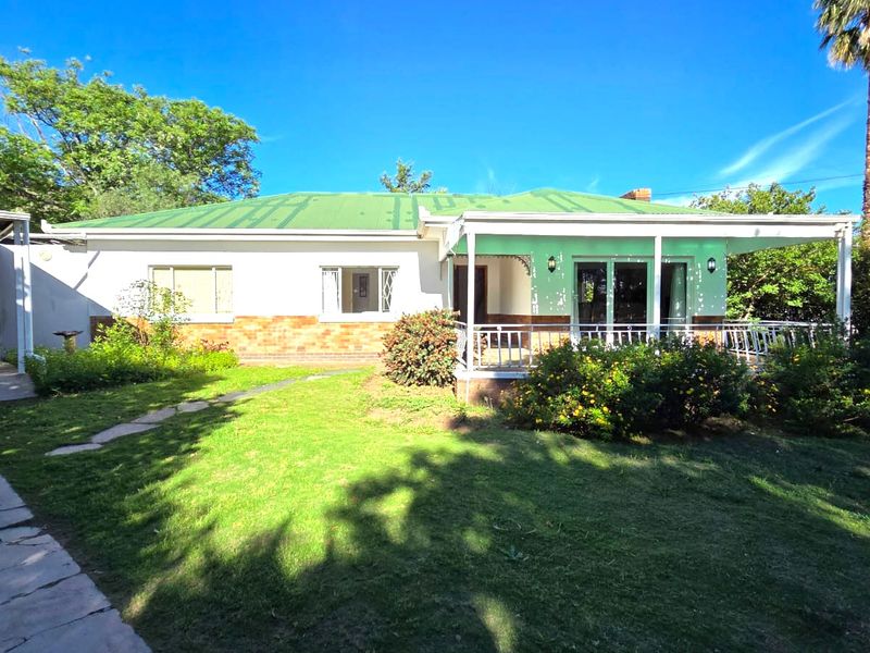 Rear view of the house featuring a covered patio, brick and plaster facade, metal roof, and an attached carport set within a garden.