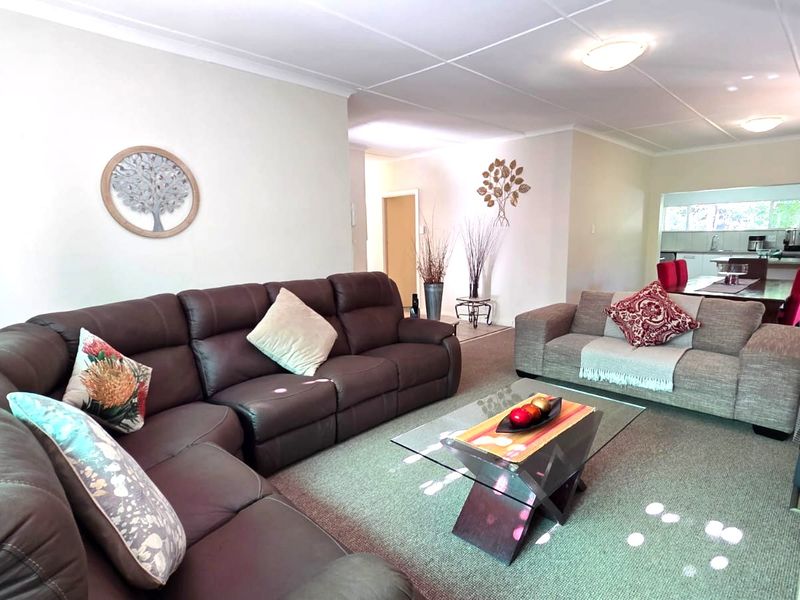 Spacious open-plan living area featuring neutral walls, tiled flooring, and integrated ceiling lighting, flowing seamlessly into the adjacent kitchen and dining space.
