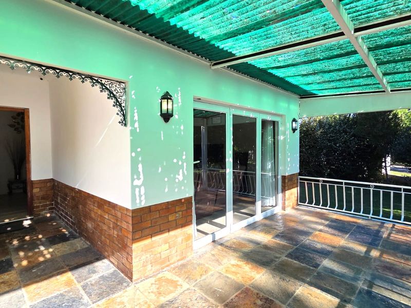 Covered patio area featuring slate tile flooring, brick base detailing, and a green corrugated roof, providing a functional outdoor entertainment space.
