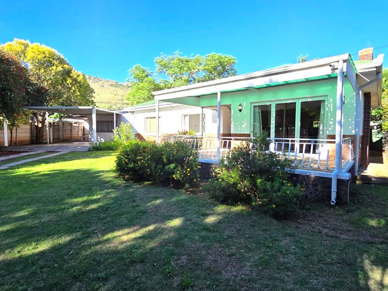 Rear view of the house featuring a covered patio, sliding glass doors, and an adjacent carport set within a spacious garden area.
