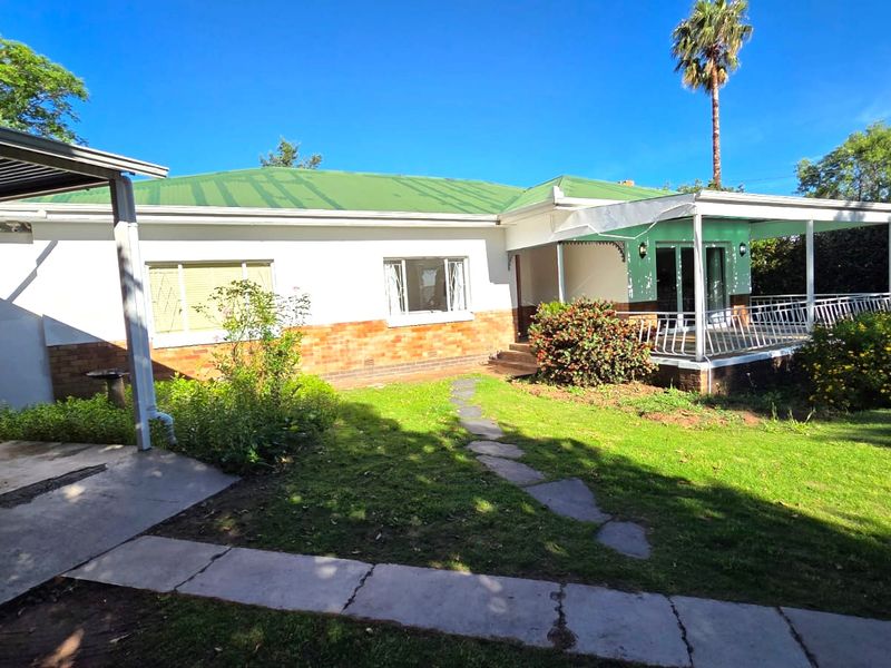 Rear view of the house featuring a green metal roof, brick and plaster facade, and a covered patio area overlooking the garden.