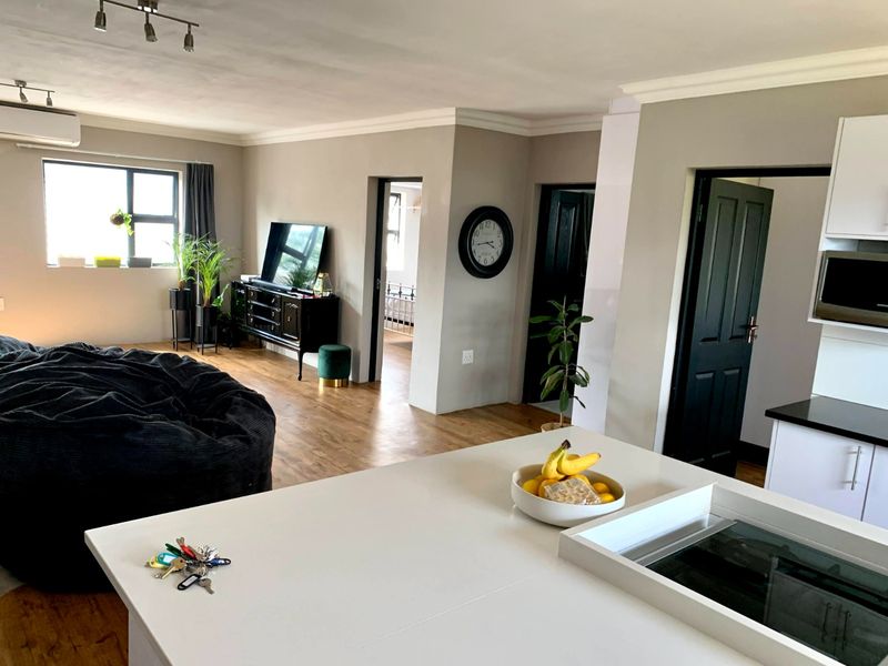 An open-plan living and kitchen area featuring modern laminate flooring, neutral wall tones, and a functional kitchen layout with built-in appliances.