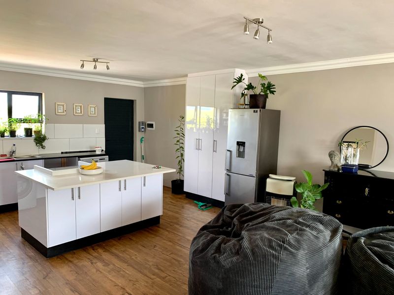A bright open-plan kitchen featuring a central island, modern white cabinetry, and laminate flooring, creating a functional and cohesive living space.