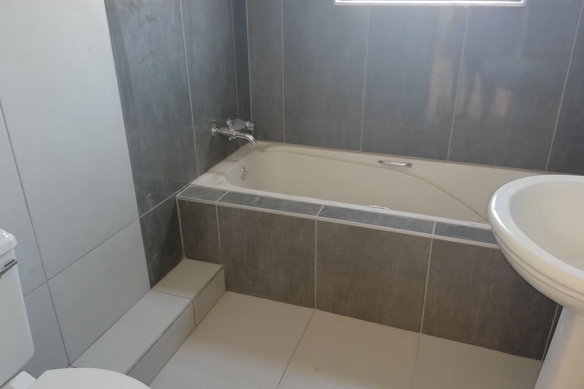 A functional bathroom featuring a built-in bathtub with chrome fixtures, a pedestal basin, and a toilet, finished with neutral wall and floor tiling.