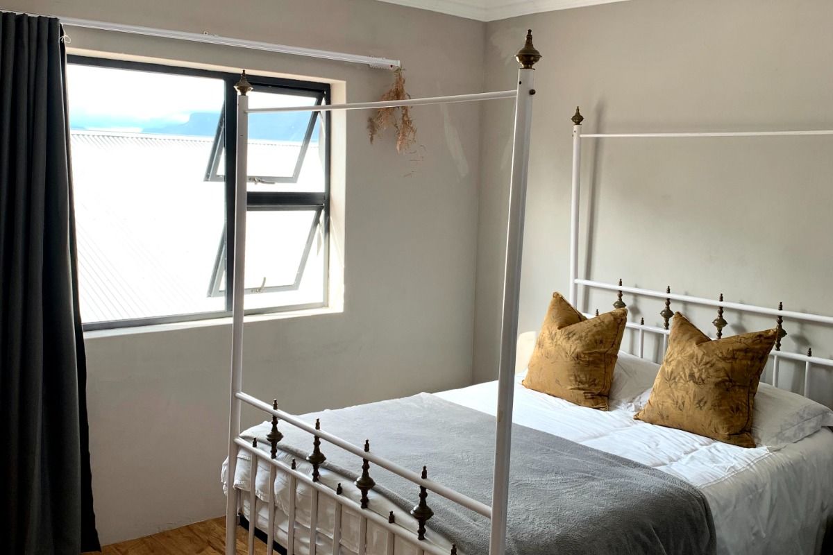 A bedroom featuring laminate flooring, ceiling cornice, and an aluminium window frame, with some visible wall paint damage requiring attention.