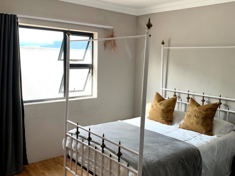 A bedroom featuring laminate flooring, ceiling cornice, and an aluminium window frame, with some visible wall paint damage requiring attention.