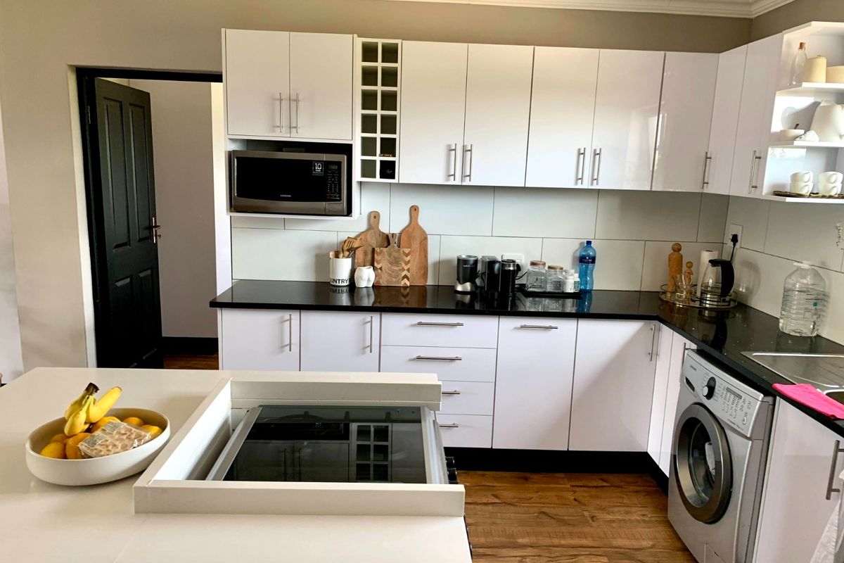 Modern kitchen featuring white cabinetry, black granite countertops, tiled backsplash, integrated microwave, and a built-in hob on the central island.