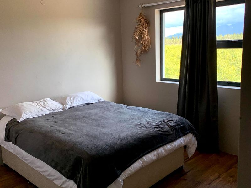 A bedroom featuring laminate flooring, coved ceilings, and an aluminium-framed window with views of the surrounding landscape.