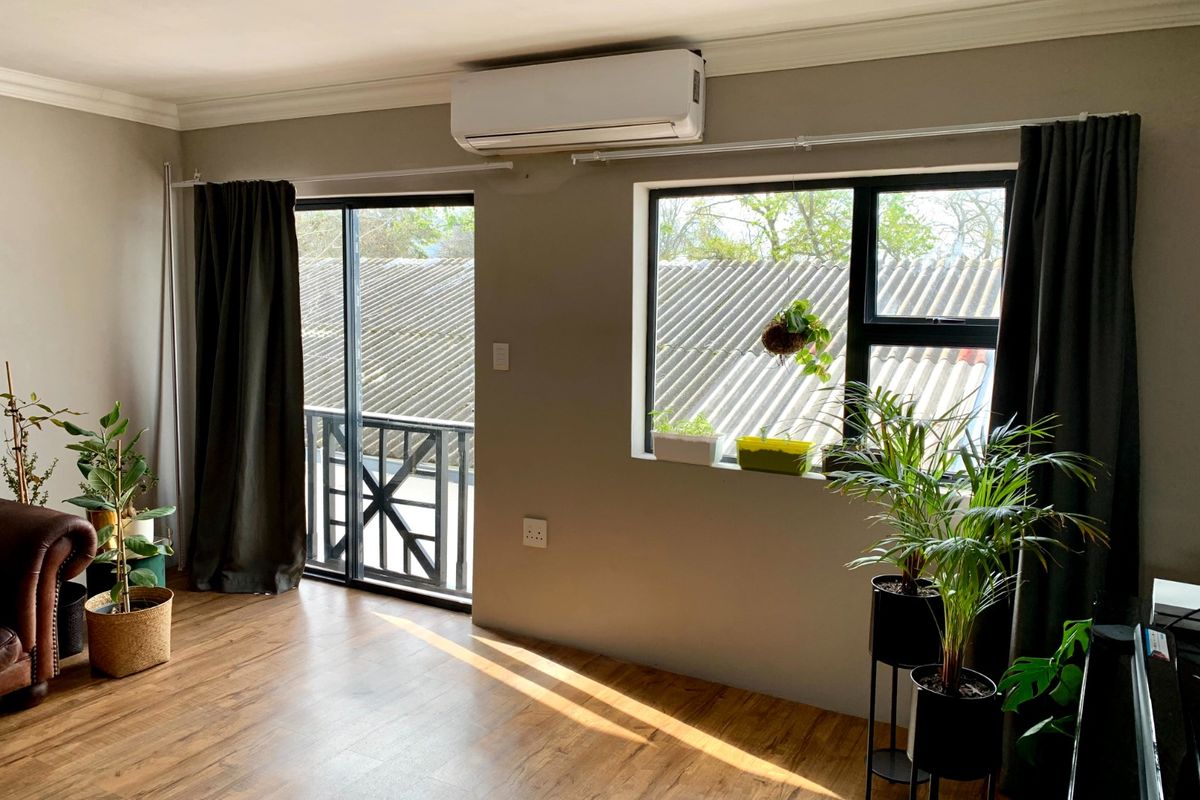 Bright living area featuring laminate flooring, a wall-mounted air conditioning unit, and access to a balcony through a sliding glass door.