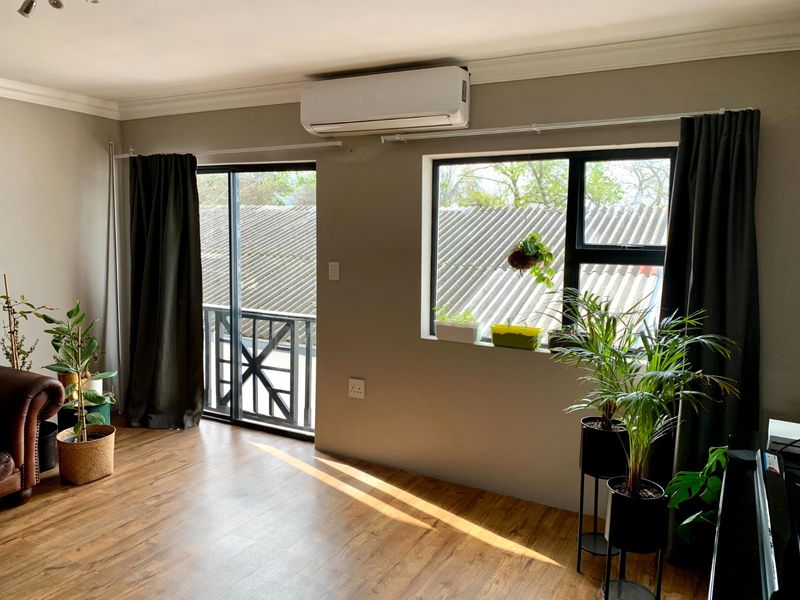 Bright living area featuring laminate flooring, a wall-mounted air conditioning unit, and access to a balcony through a sliding glass door.