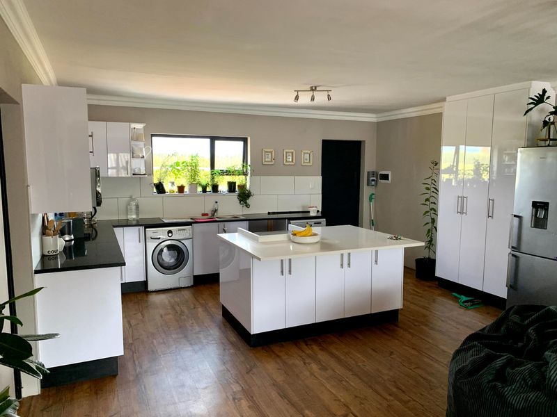 Modern kitchen featuring a central island, sleek white cabinetry, dark countertops, and integrated appliances, finished with warm wood-look flooring.