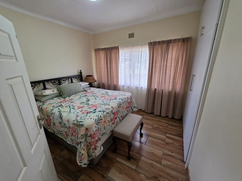A well-maintained bedroom featuring wood-look tiled flooring, built-in cupboards, and decorative ceiling cornicing, offering a clean and functional living space.