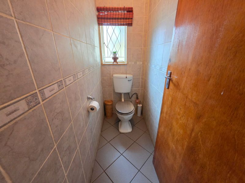 A compact guest bathroom featuring full-height ceramic wall tiling, tiled flooring, and a standard toilet suite.