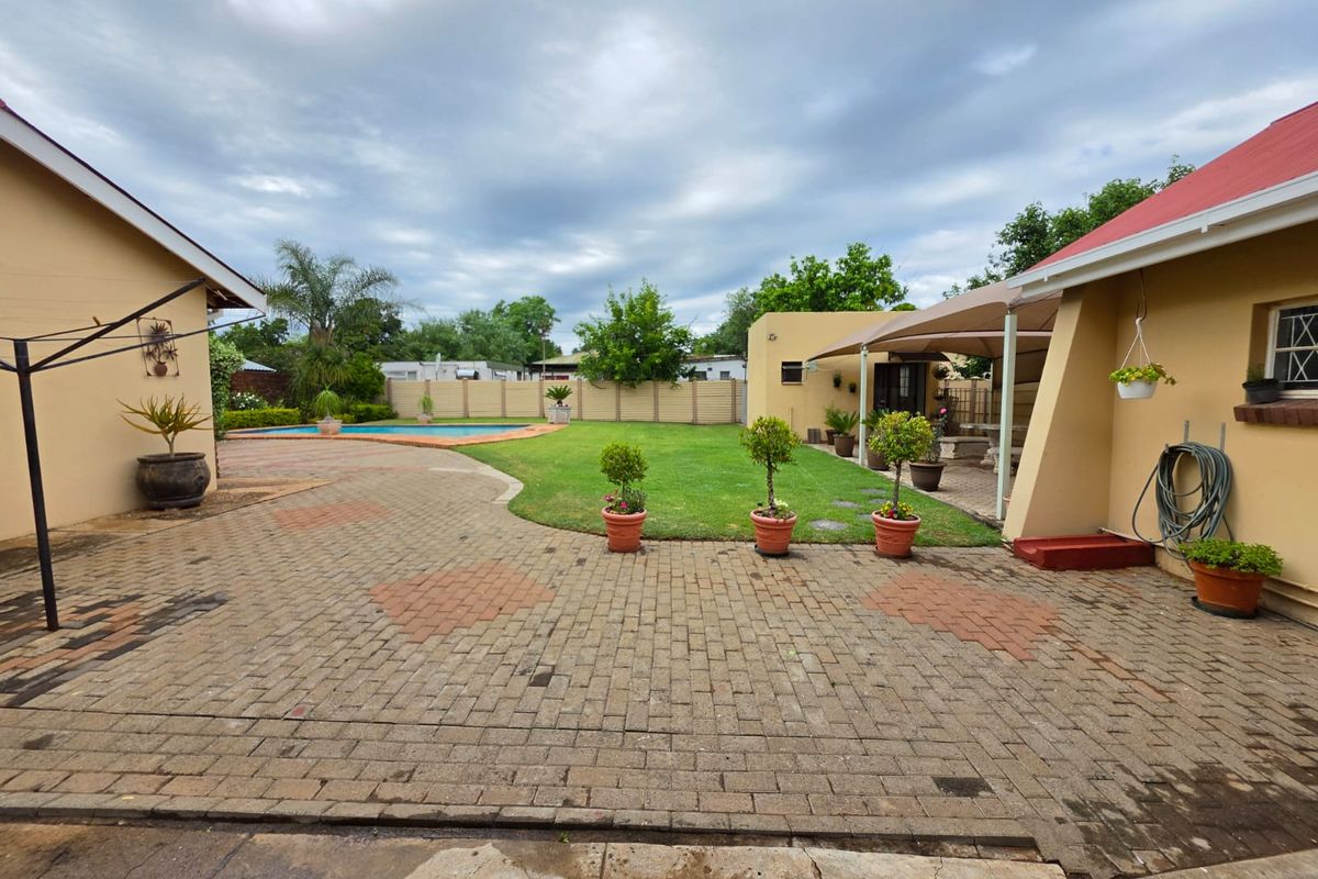 Spacious rear garden featuring a paved patio area, a swimming pool, and a covered outdoor entertainment space.