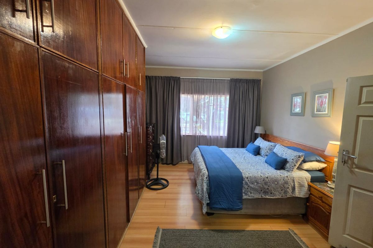 A well-maintained bedroom featuring extensive built-in wooden cabinetry, laminate flooring, and neutral wall tones, offering a functional and comfortable living space.