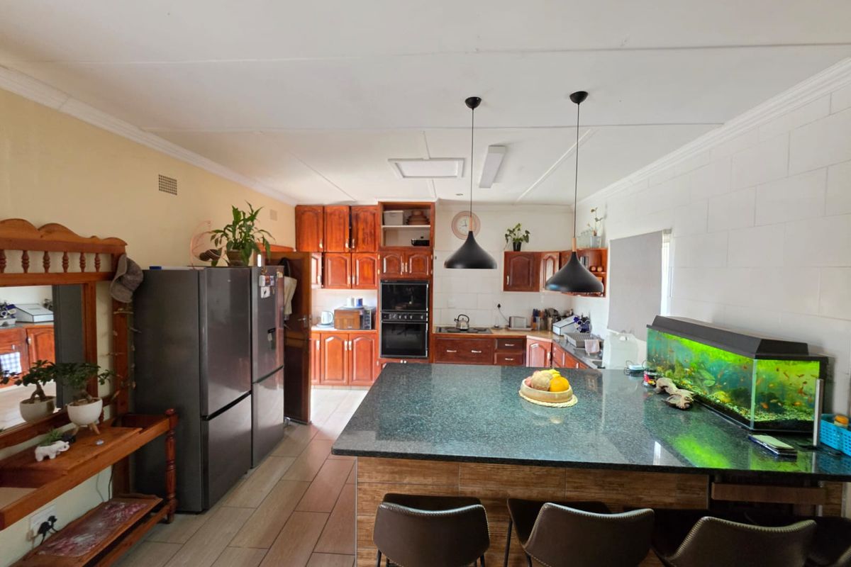 Spacious kitchen featuring wooden cabinetry, a large granite-topped island, built-in oven, and tiled flooring, offering a functional layout for cooking and casual dining.