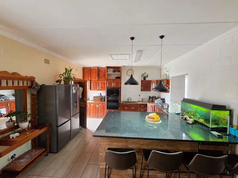 Spacious kitchen featuring wooden cabinetry, a large granite-topped island, built-in oven, and tiled flooring, offering a functional layout for cooking and casual dining.