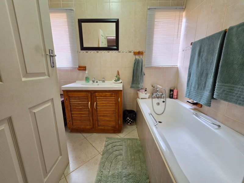 A functional bathroom featuring a wooden vanity cabinet, a bathtub with a mixer tap, and neutral wall and floor tiling.