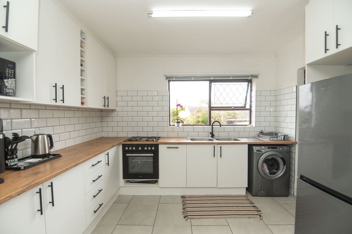 Modern kitchen featuring white cabinetry, wooden countertops, subway tile backsplash, built-in oven, electric hob, and integrated laundry facilities.