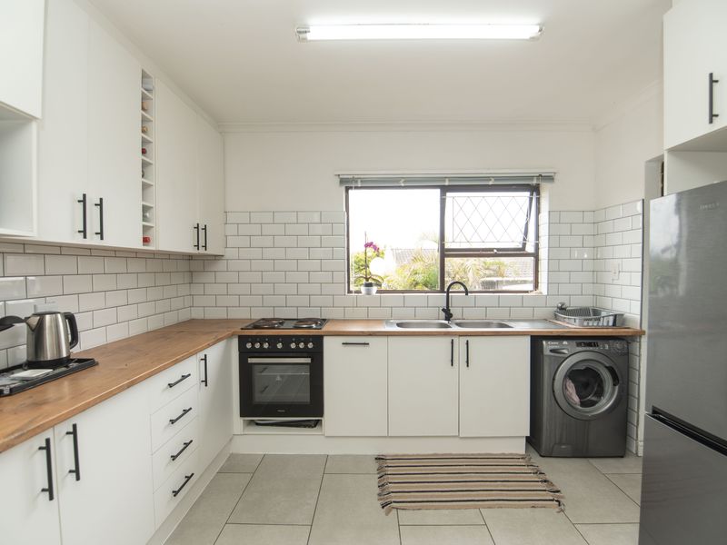 Modern kitchen featuring white cabinetry, wooden countertops, subway tile backsplash, built-in oven, electric hob, and integrated laundry facilities.