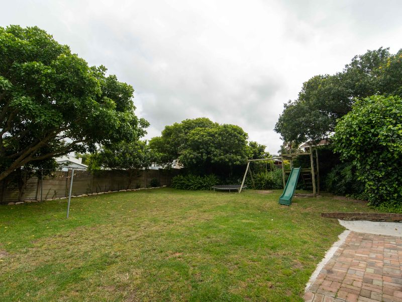 A spacious private backyard featuring a well-maintained lawn, mature trees, brick paved area, and perimeter boundary walling.
