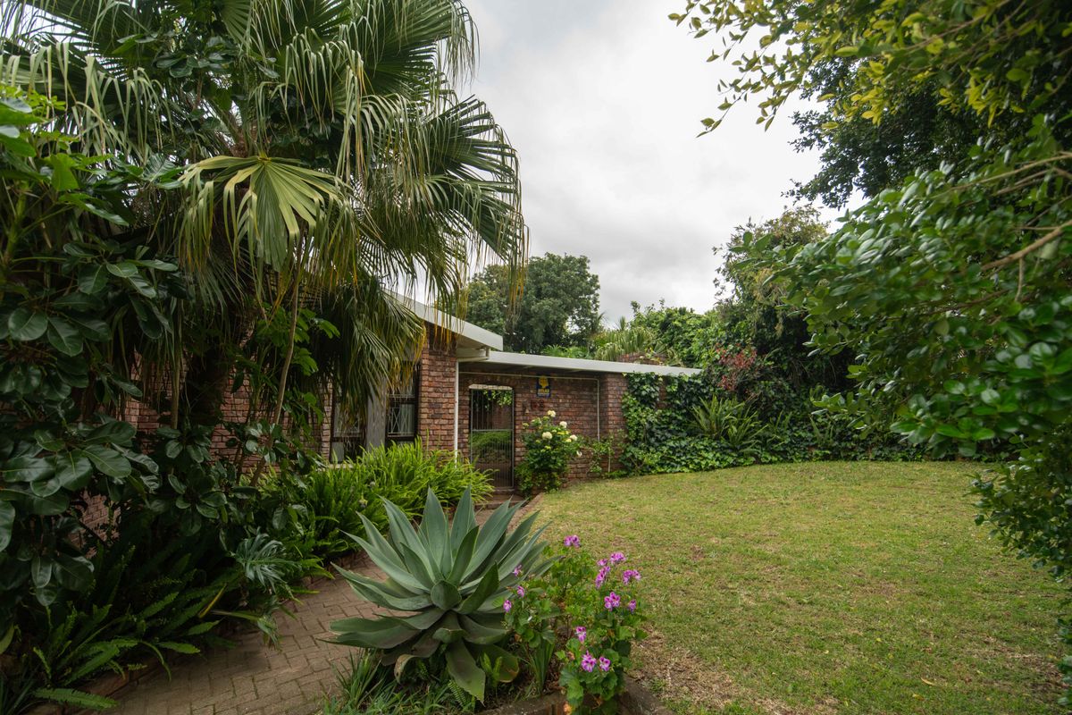 A private rear garden featuring a brick facade, established landscaping, a paved walkway, and a secure gated entrance.