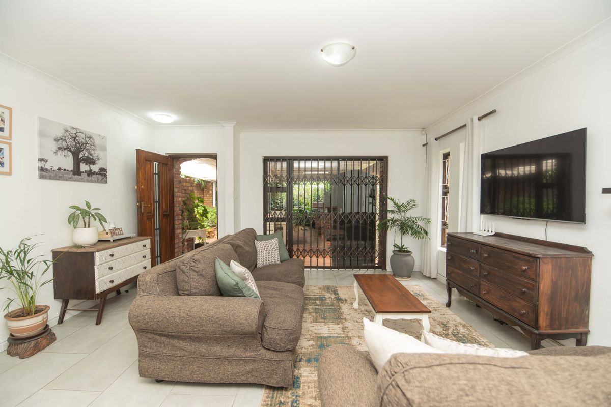 A bright and well-maintained living room featuring tiled flooring, a security gate leading to the patio, and neutral wall finishes.