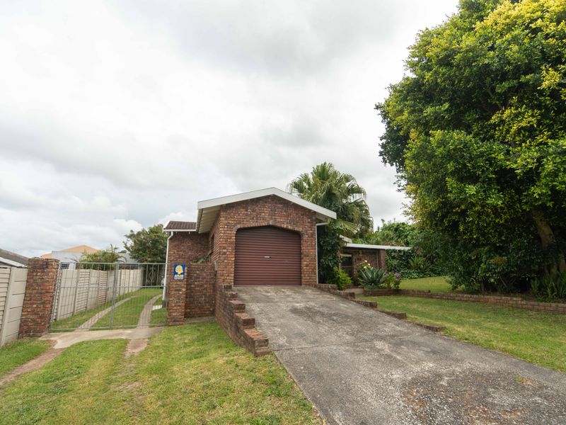 Front exterior view of a brick house featuring a single garage, concrete driveway, and enclosed garden area with boundary walling.