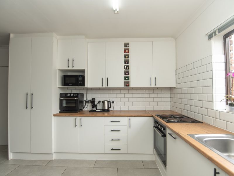 Modern kitchen featuring white cabinetry, subway tile backsplash, wooden countertops, built-in oven, electric hob, and a stainless steel sink.