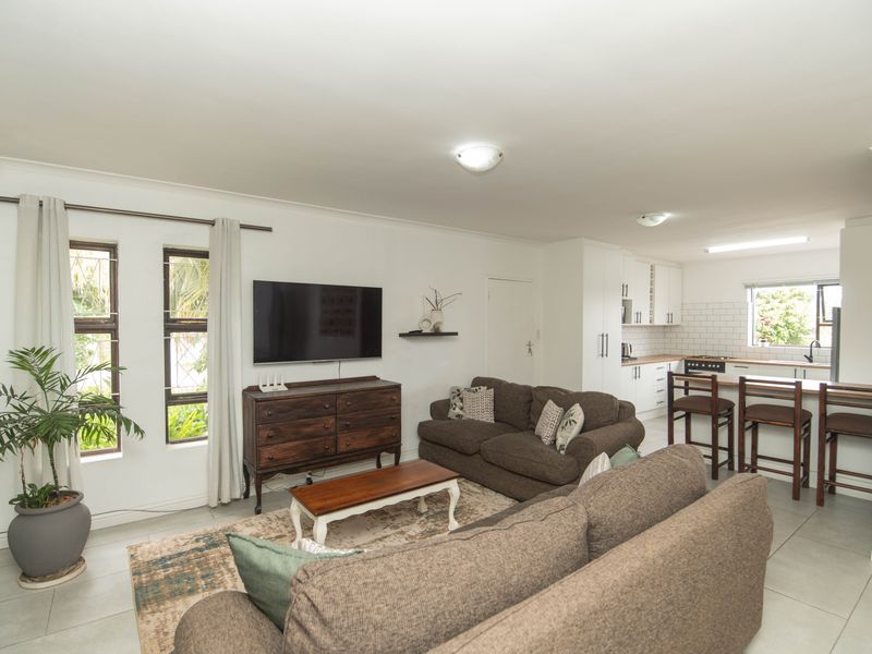 An open-plan living and kitchen area featuring tiled floors, a modern kitchen with subway tile backsplash, and a breakfast bar.