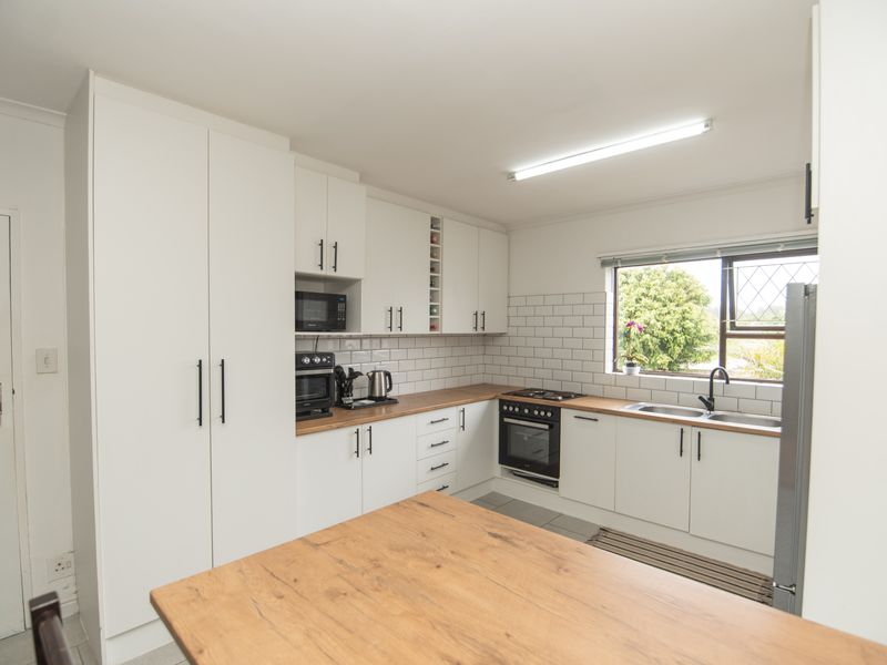 A clean, modern kitchen featuring white cabinetry, subway tile backsplash, wooden countertops, and integrated cooking appliances with ample natural light.