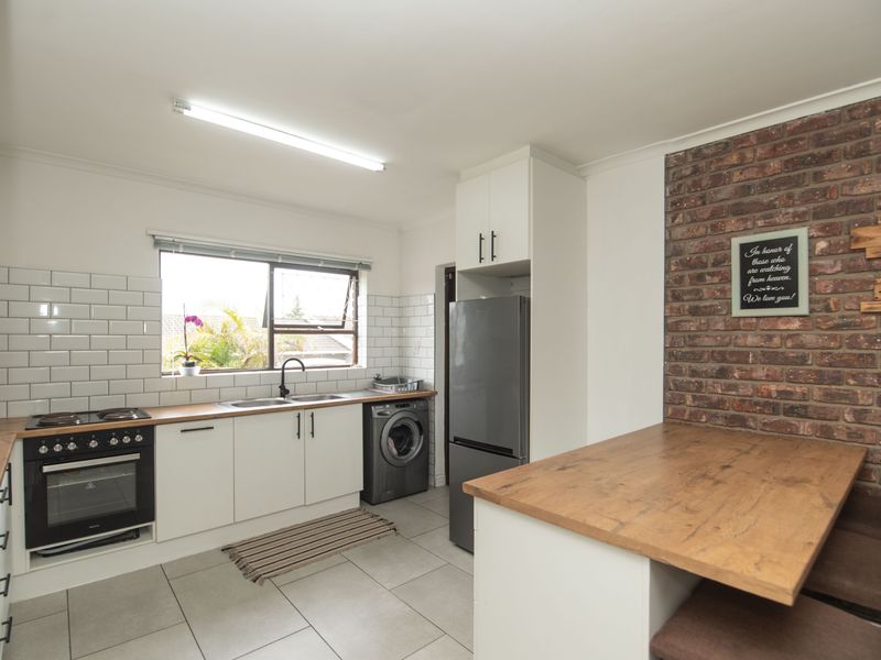 Modern kitchen featuring white cabinetry, wooden countertops, subway tile backsplash, and an exposed brick feature wall with integrated oven and hob.