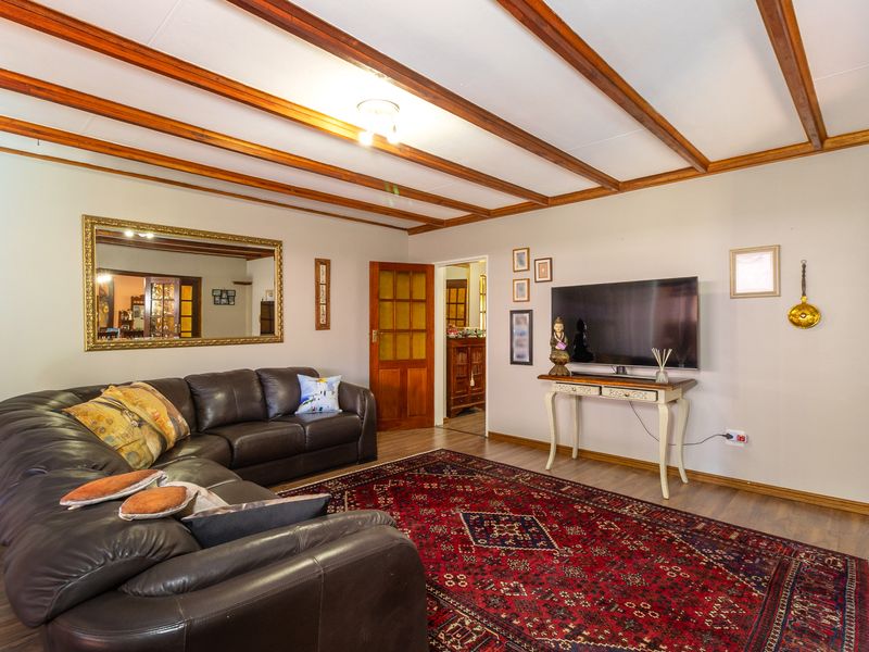 A comfortable living room featuring exposed timber ceiling beams, laminate flooring, and classic timber-framed glass panel doors.