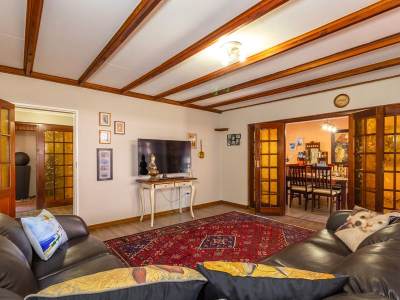 Spacious living room featuring exposed timber ceiling beams, laminate flooring, and classic timber-framed glass panel doors leading to adjacent rooms.
