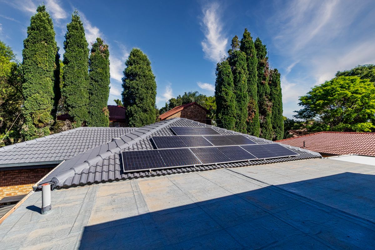 An elevated view of the property roof featuring a solar panel installation on a tiled roof section and a flat roof area.