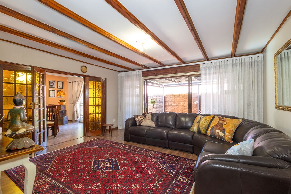 Spacious living room featuring exposed timber ceiling beams, laminate flooring, and sliding glass doors providing access to the outdoor patio area.