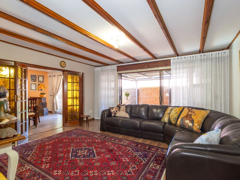Spacious living room featuring exposed timber ceiling beams, laminate flooring, and sliding glass doors providing access to the outdoor patio area.