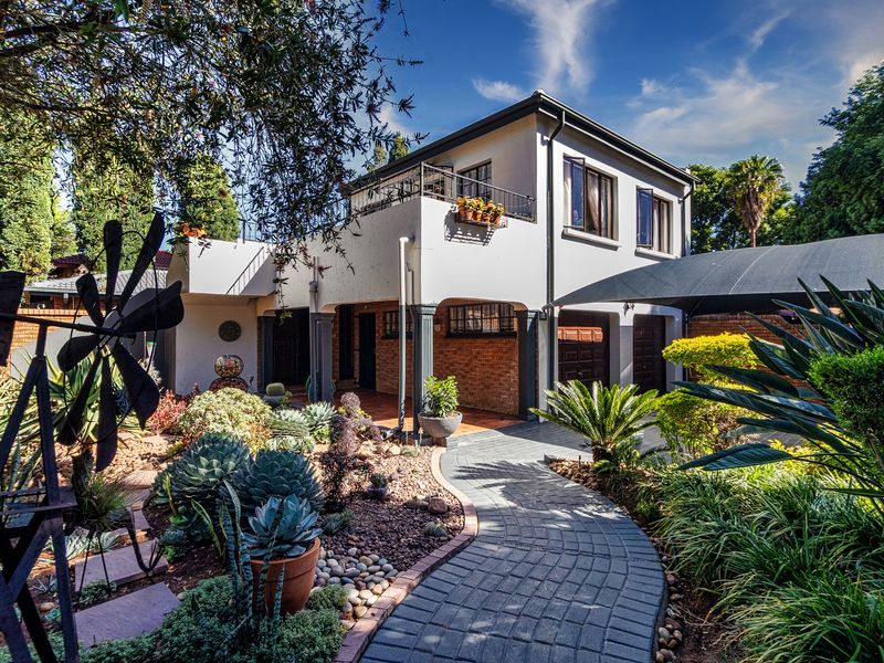 A well-maintained double-story duet property featuring a paved walkway, landscaped garden, and a balcony overlooking the front entrance and garage area.