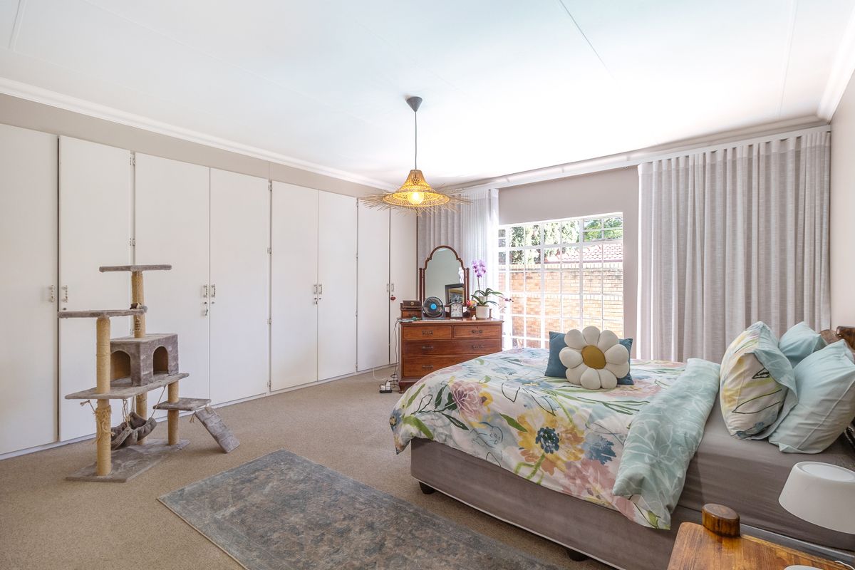 A spacious bedroom featuring extensive built-in cupboards, neutral carpeting, and large windows with curtain tracks, offering a comfortable and functional living space.