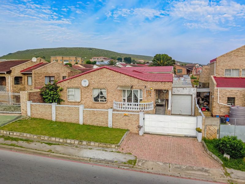 An elevated view of a face-brick residential property featuring a tiled roof, paved driveway, secure boundary wall, and integrated garage.