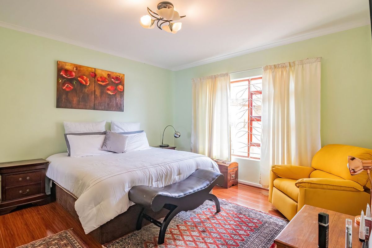 A well-lit bedroom featuring laminate flooring, a window with security bars, and a central ceiling light fixture.